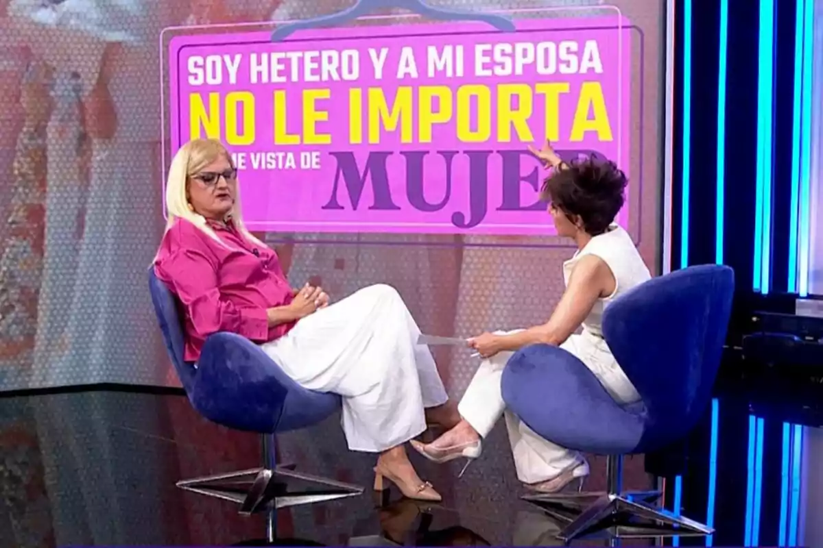 Dos personas están sentadas en Y ahora Sonsoles, una de ellas lleva una peluca rubia y ropa rosa, mientras que Sonsoles Ónega viste de blanco. Detrás de ellas hay un cartel con texto en colores llamativos. Dos personas están sentadas en Y ahora Sonsoles, una de ellas lleva una peluca rubia y ropa rosa, mientras que Sonsoles Ónega viste de blanco. Detrás de ellas hay un cartel con texto en colores llamativos.