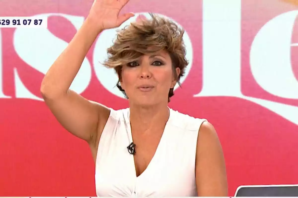 Sonsoles Ónega amb cabell curt i despentinat, vestida amb una brusa blanca sense mànigues, aixeca la mà mentre està en un set de televisió amb un fons vermell i blanc a Y ahora Sonsoles Sonsoles Ónega amb cabell curt i despentinat, vestida amb una brusa blanca sense mànigues, aixeca la mà mentre està en un set de televisió amb un fons vermell i blanc a Y ahora Sonsoles