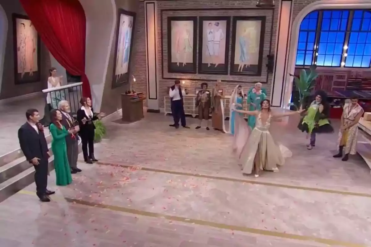 Los concursantes de 'Maestros de la Costura Celebrity' elegantemente vestidos se encuentra en un salón amplio con decoraciones artísticas en las paredes, mientras una mujer en el centro parece estar realizando una presentación o baile, rodeada de pétalos en el suelo. Los concursantes de 'Maestros de la Costura Celebrity' elegantemente vestidos se encuentra en un salón amplio con decoraciones artísticas en las paredes, mientras una mujer en el centro parece estar realizando una presentación o baile, rodeada de pétalos en el suelo.