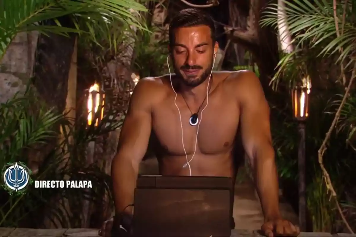 Borja González sin camisa está usando auriculares y mirando una pantalla en un entorno selvático iluminado por antorchas. Captura de 'Supervivientes' Borja González sin camisa está usando auriculares y mirando una pantalla en un entorno selvático iluminado por antorchas. Captura de 'Supervivientes'