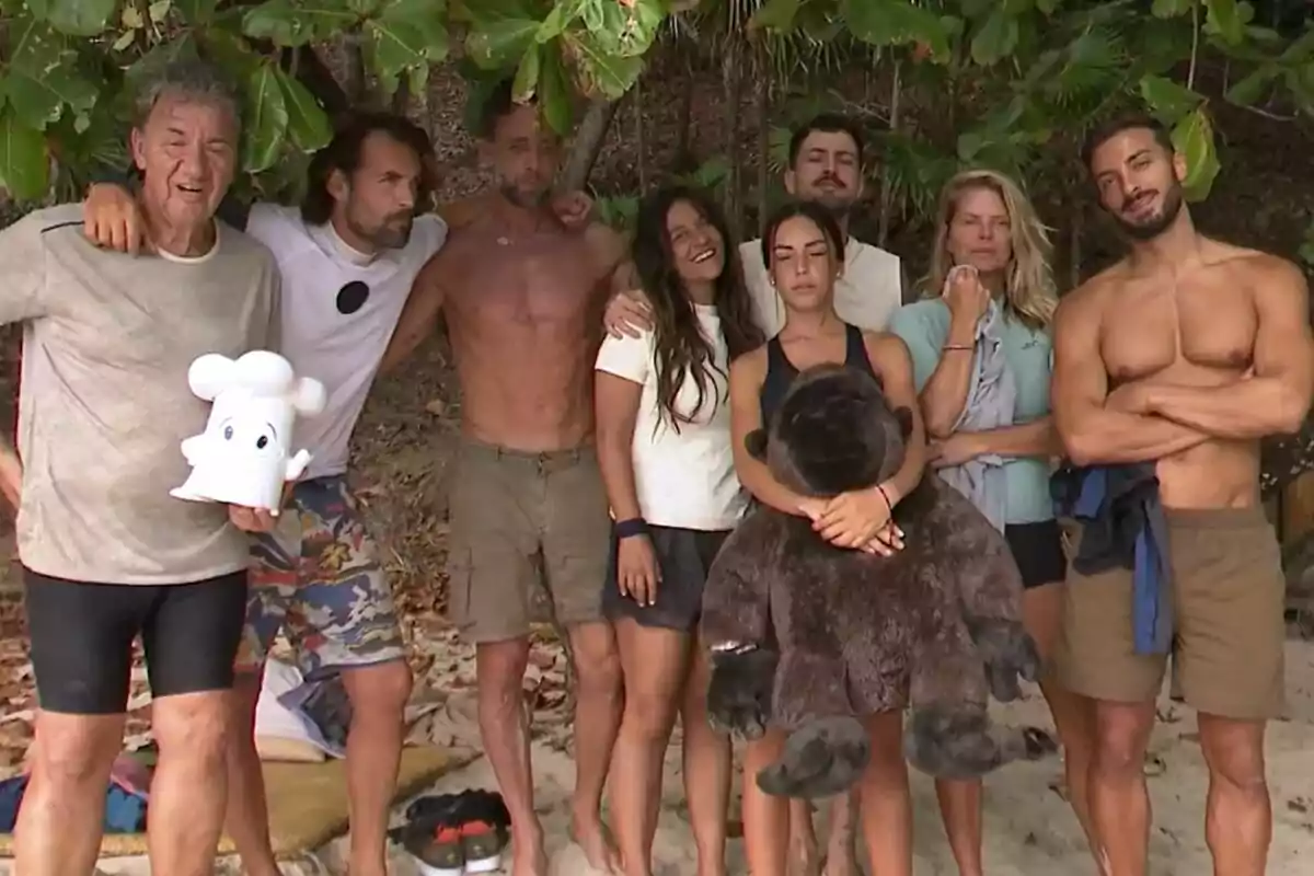 Un grup de persones format per Koldo Royo, Álex Adrover, Álvaro Muñoz Escassi, Laura Cuevas, Joshua Velázquez, Anita Williams, Makoke i Borja González posant juntes en una platja, algunes d'elles abraçades i una persona sostenint un peluix gran, amb vegetació de fons a Supervivientes.