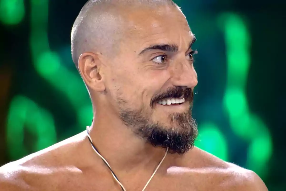 Damián Quintero somriu mirant cap a la dreta amb un fons desenfocat de llums verdes. Captura de 'Supervivientes'