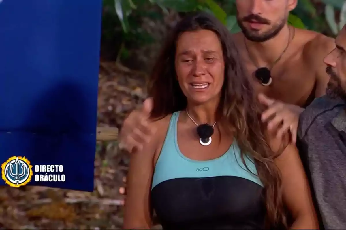 Laura Cuevas llorando mientras es consolada por dos personas en un entorno al aire libre con un cartel que dice "Directo Oráculo". Captura de 'Supervivientes'
