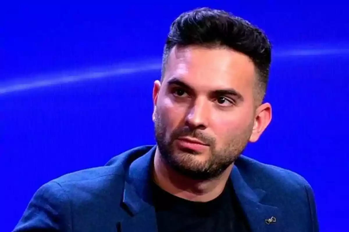 Suso Álvarez con barba y cabello oscuro viste una chaqueta azul sobre una camiseta negra con un fondo azul en GH DÚO.