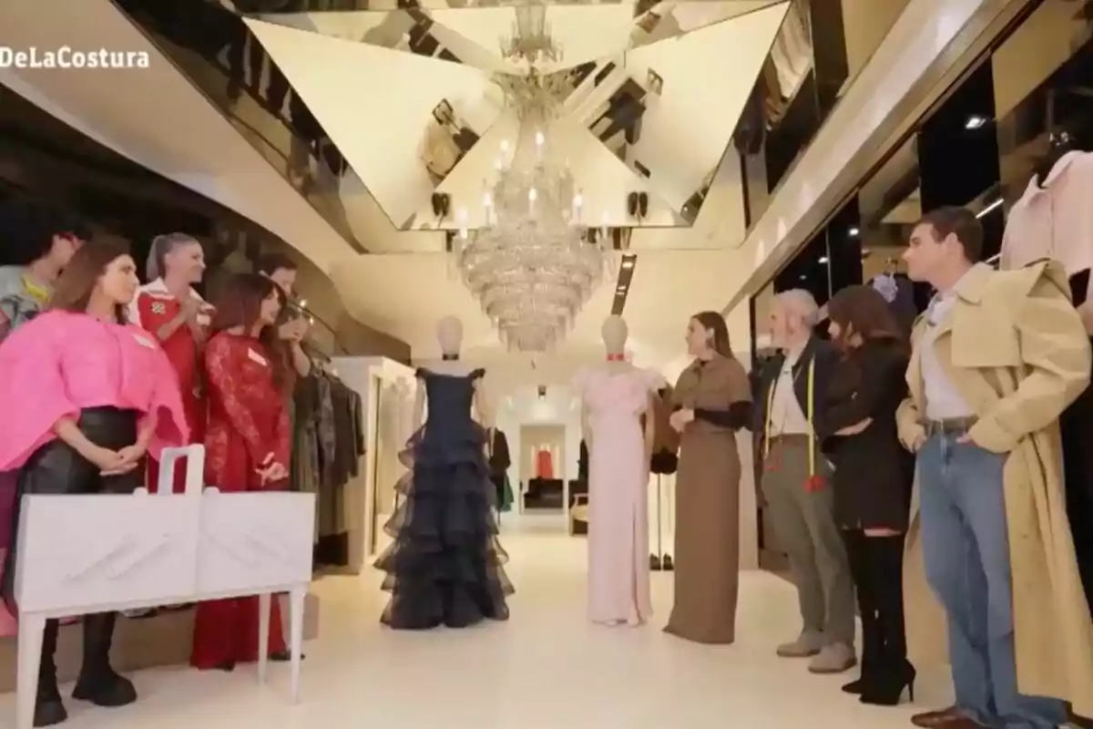 El jurado y los concursantes observan dos maniquíes vestidos en un entorno elegante con un candelabro y espejos en el techo en 'Maestros de la Costura Celebrity'. El jurado y los concursantes observan dos maniquíes vestidos en un entorno elegante con un candelabro y espejos en el techo en 'Maestros de la Costura Celebrity'.