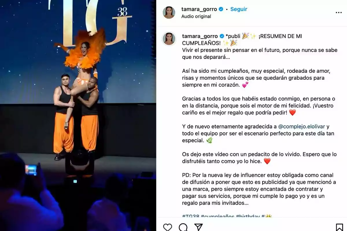 Tamara Gorro con un atuendo naranja y plumas es levantada por dos hombres en un escenario, con un fondo que muestra las letras Tamara Gorro con un atuendo naranja y plumas es levantada por dos hombres en un escenario, con un fondo que muestra las letras