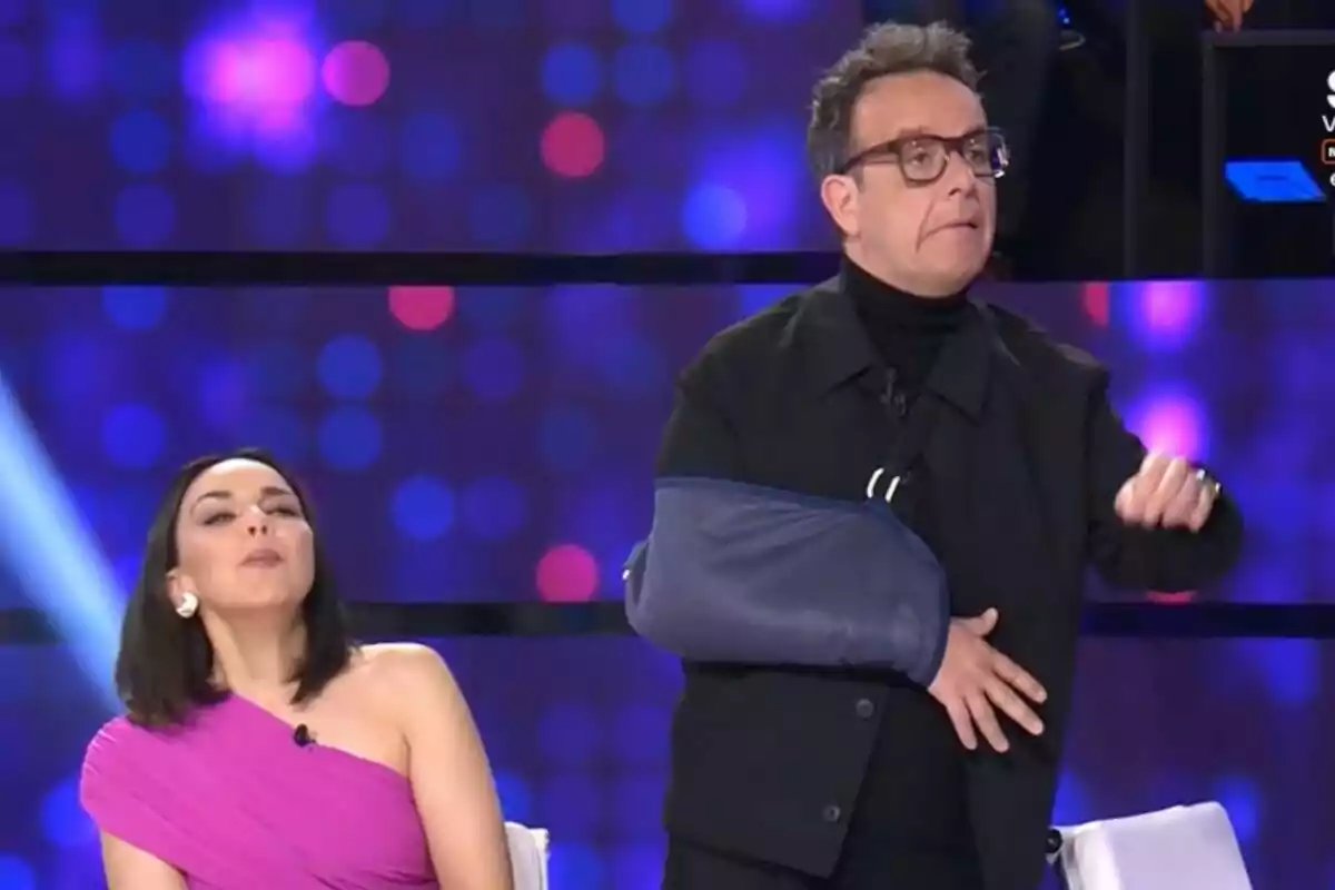Chenoa amb vestit rosa i Àngel Llàcer amb cabestrell al braç són en un escenari amb llums de fons a 'Tu cara me suena'. Chenoa amb vestit rosa i Àngel Llàcer amb cabestrell al braç són en un escenari amb llums de fons a 'Tu cara me suena'.