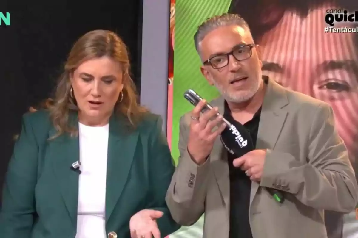 Carlota Corredera y Kiko Hernández en un set de televisión, una mujer con chaqueta verde y un hombre con chaqueta beige, sosteniendo un micrófono en 'Tentáculos'. Carlota Corredera y Kiko Hernández en un set de televisión, una mujer con chaqueta verde y un hombre con chaqueta beige, sosteniendo un micrófono en 'Tentáculos'.