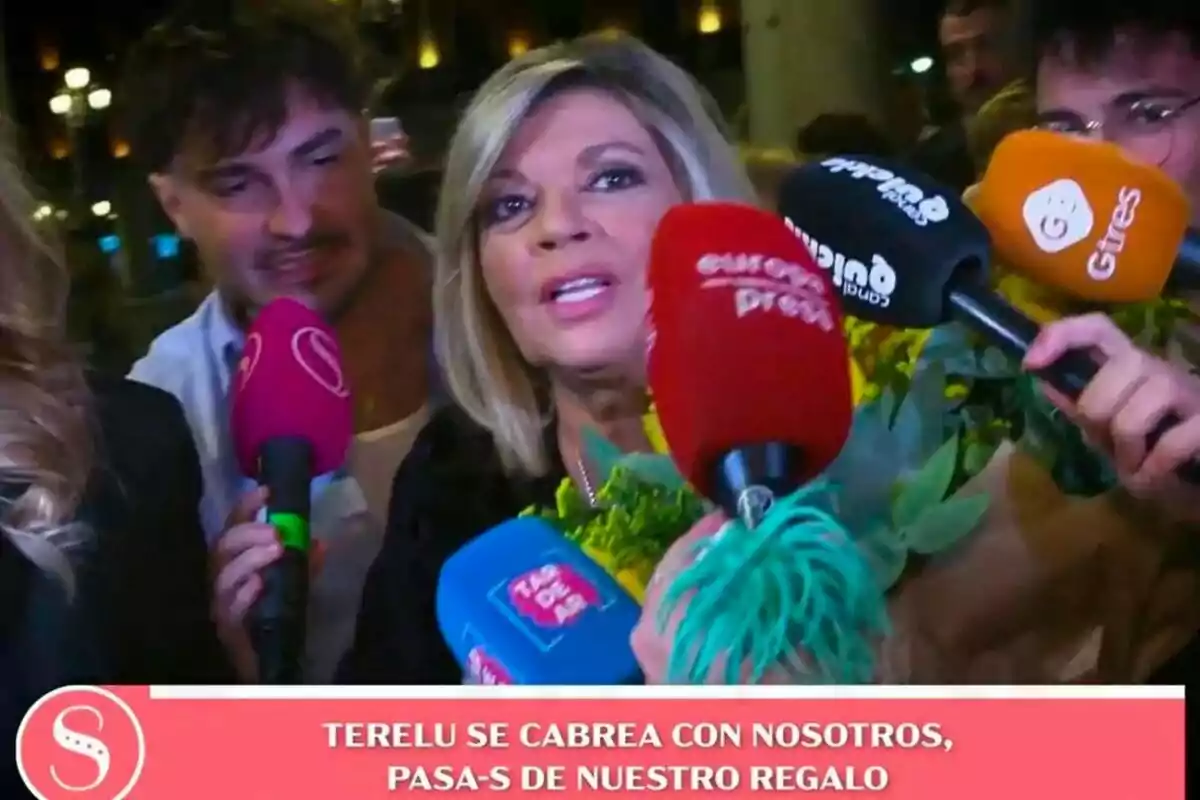 Terelu Campos rodeada de micrófonos de diferentes medios de comunicación mientras sostiene un ramo de flores en Socialité. Terelu Campos rodeada de micrófonos de diferentes medios de comunicación mientras sostiene un ramo de flores en Socialité.