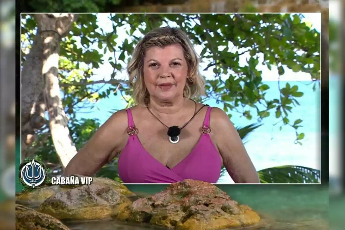 Terelu Campos durante su intervención en 'Supervivientes' con vestido rosa posa frente a un fondo de vegetación y mar, con el logo de Terelu Campos durante su intervención en 'Supervivientes' con vestido rosa posa frente a un fondo de vegetación y mar, con el logo de
