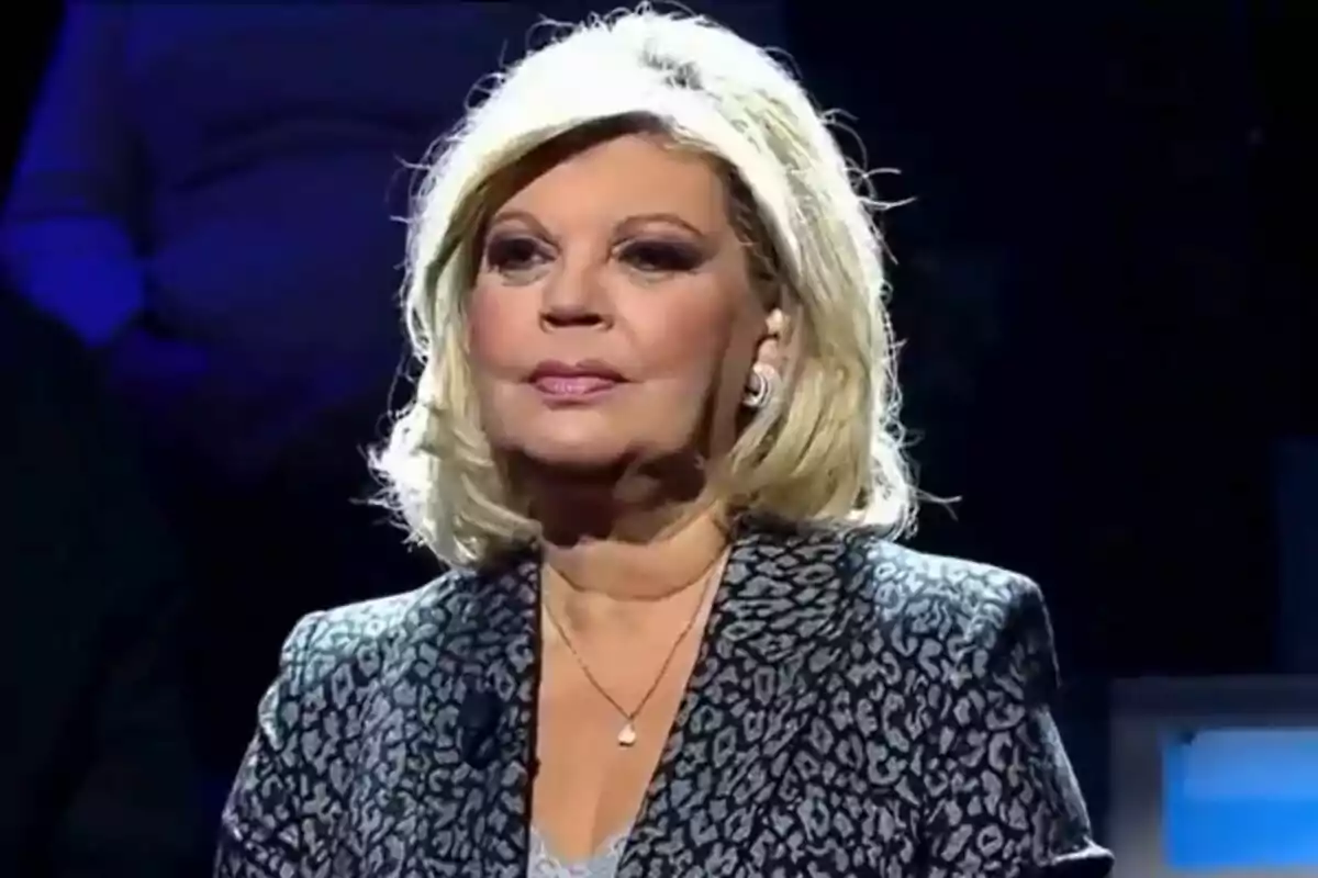 Terelu Campos con cabello rubio y maquillaje elegante lleva un traje con estampado mientras está en un entorno con iluminación tenue en De Viernes. Terelu Campos con cabello rubio y maquillaje elegante lleva un traje con estampado mientras está en un entorno con iluminación tenue en De Viernes.