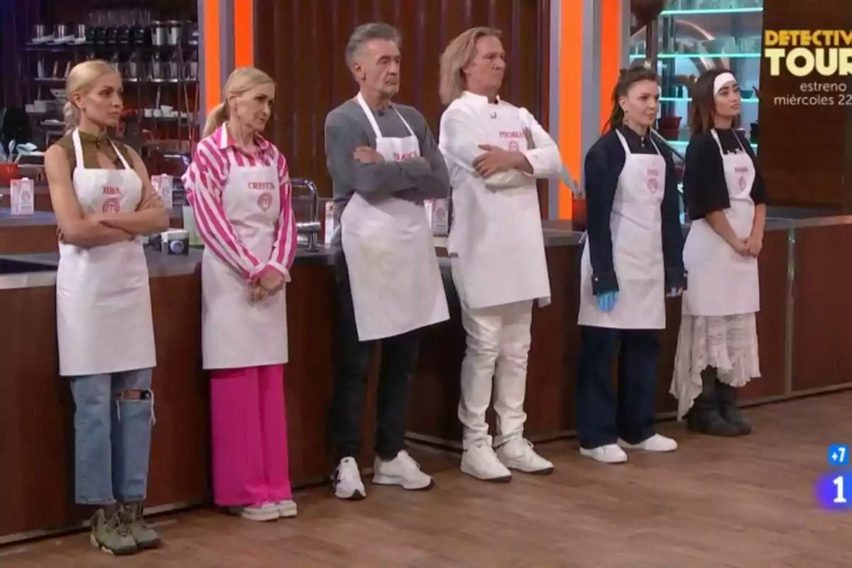 Concursantes de MasterChef Celebrity como Cristina Cifuentes, Hiba Abouk, Francis Lorenzo, Inés Hernand, Marina Rivers y Pocholo con delantales blancos está de pie en una cocina. Concursantes de MasterChef Celebrity como Cristina Cifuentes, Hiba Abouk, Francis Lorenzo, Inés Hernand, Marina Rivers y Pocholo con delantales blancos está de pie en una cocina.