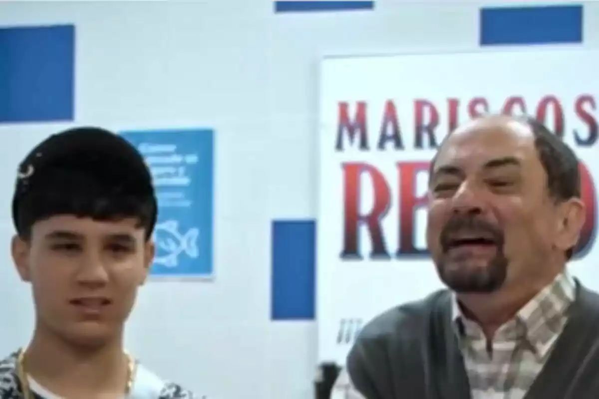 Jordi Sánchez como Antonio Recio junto a su hijo Toñín en un lugar con un cartel de Mariscos Rocio en el fondo en La que se avecina. Jordi Sánchez como Antonio Recio junto a su hijo Toñín en un lugar con un cartel de Mariscos Rocio en el fondo en La que se avecina.