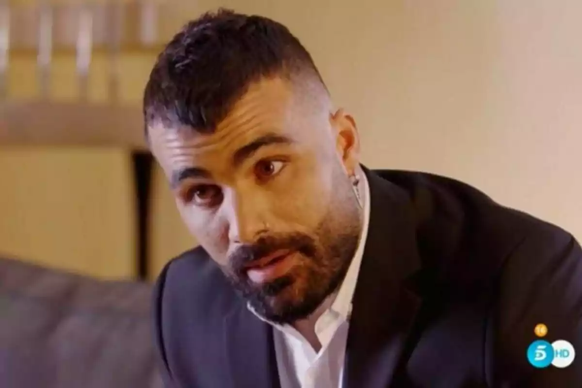 Tutto Durán con barba y cabello corto lleva un traje oscuro y una camisa blanca mientras mira hacia adelante en un entorno interior.