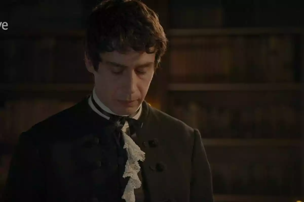 Julio con los ojos cerrados, vestido con ropa de época oscura y una corbata de encaje, en una biblioteca. Captura de 'Valle Salvaje' Julio con los ojos cerrados, vestido con ropa de época oscura y una corbata de encaje, en una biblioteca. Captura de 'Valle Salvaje'