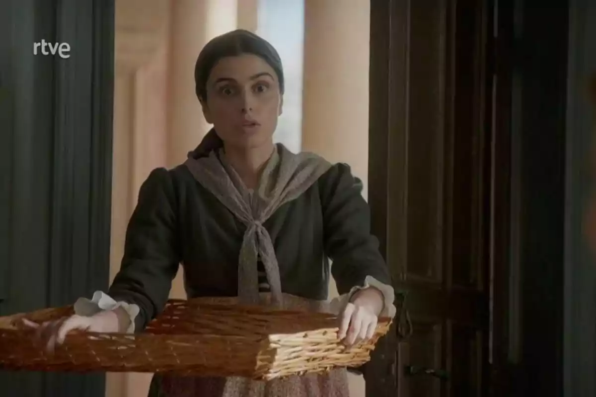 Matilde vestida con ropa de época sostiene una canasta de mimbre mientras está de pie en una puerta. Captura de 'Valle Salvaje' Matilde vestida con ropa de época sostiene una canasta de mimbre mientras está de pie en una puerta. Captura de 'Valle Salvaje'