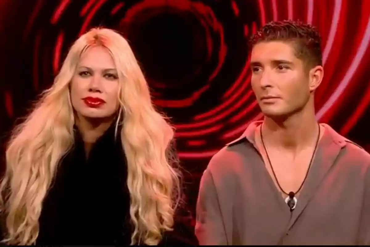 Vanessa Bouza i Álex Ghita assegudes davant d'un fons vermell amb un disseny circular a GH DÚO.