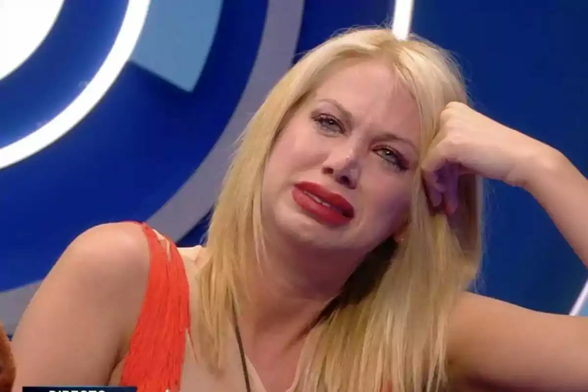 Vanessa Bouza rossa amb expressió de tristesa i llàgrimes als ulls, recolzant el seu cap a la mà, amb un fons blau a GH DÚO.