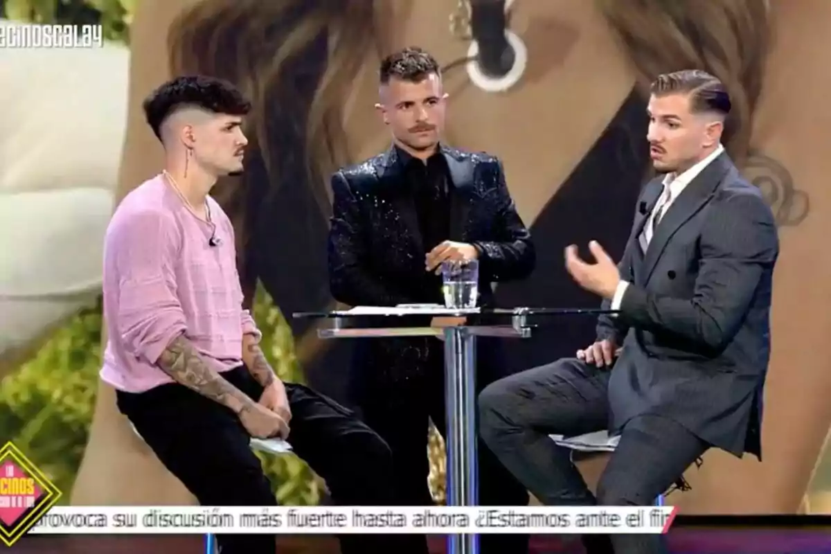 Álvaro, Tadeo e Iban García están sentados y de pie alrededor de una mesa alta en un set de televisión, uno de ellos lleva un traje brillante, otro una camiseta rosa y el tercero un traje gris, mientras conversan en un programa. Álvaro, Tadeo e Iban García están sentados y de pie alrededor de una mesa alta en un set de televisión, uno de ellos lleva un traje brillante, otro una camiseta rosa y el tercero un traje gris, mientras conversan en un programa.