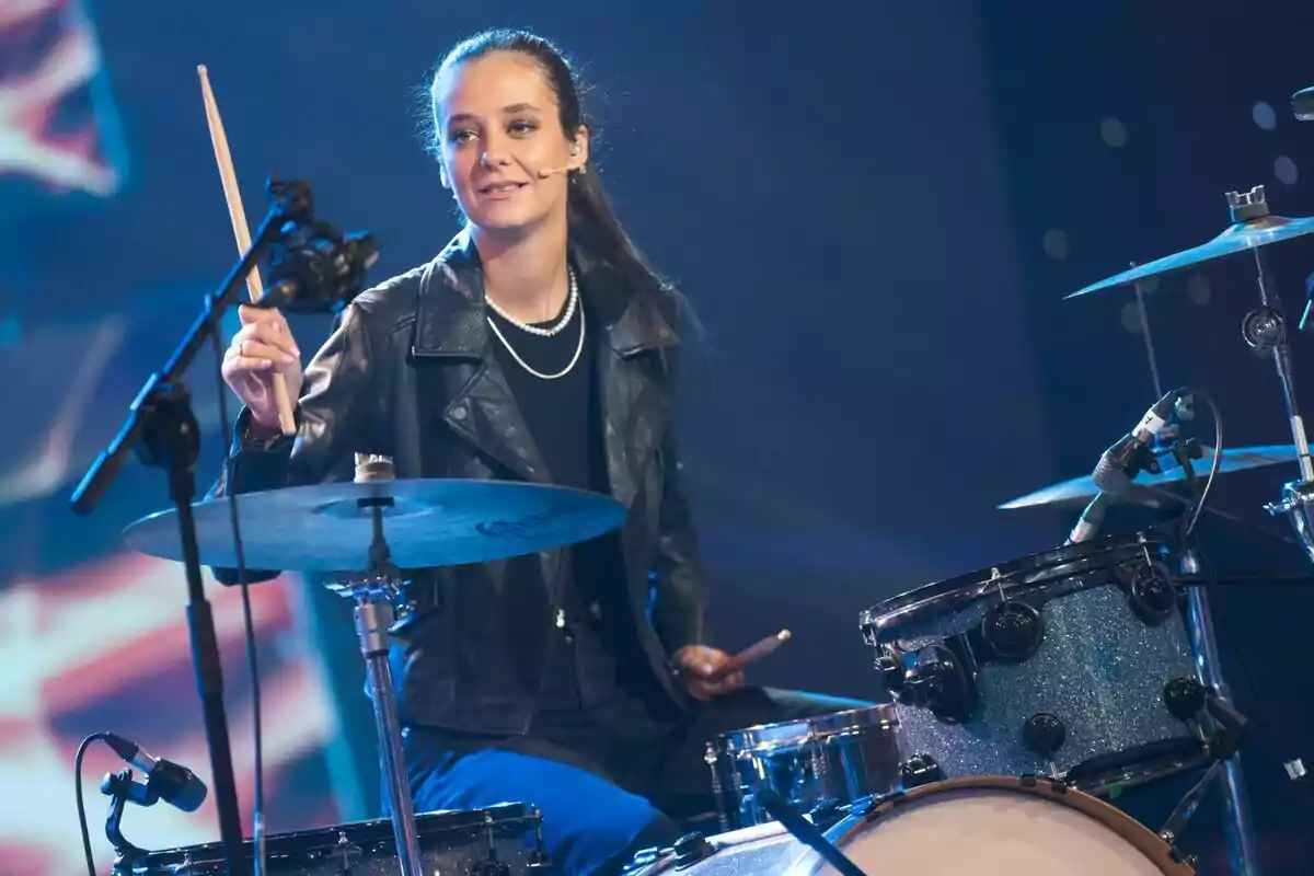 Victoria Federica tocando la batería en un escenario con luces de fondo en El Desafío. Victoria Federica tocando la batería en un escenario con luces de fondo en El Desafío.