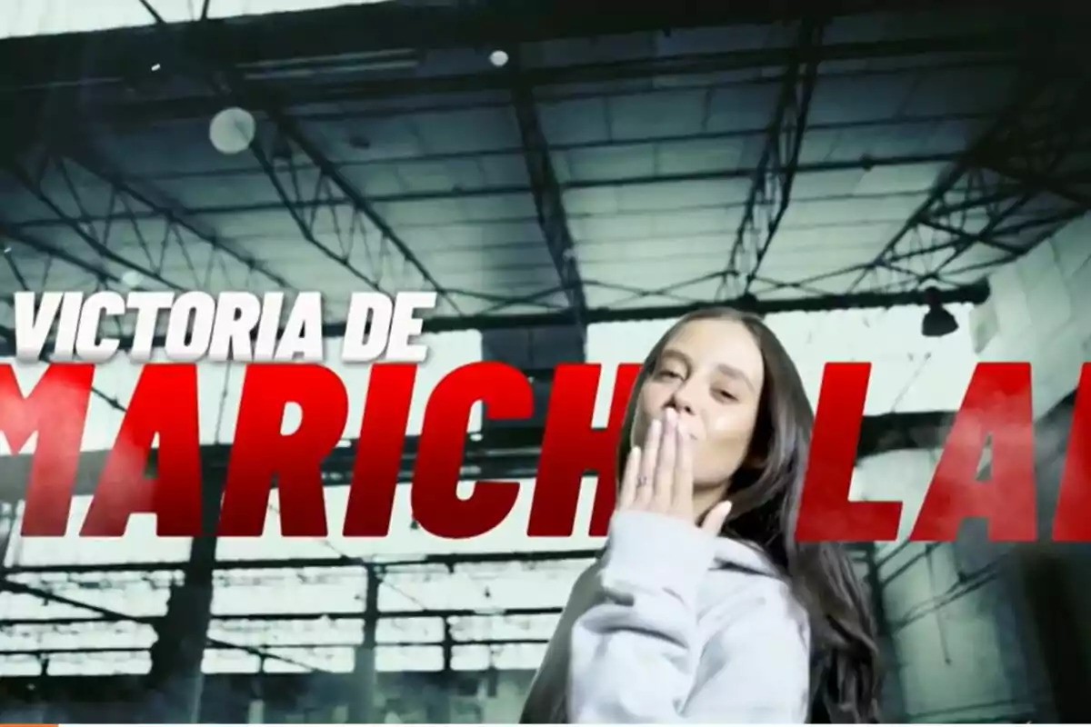 Victoria Federica con cabello largo y oscuro lanza un beso frente a un fondo industrial con texto grande en rojo y blanco de El Desafío. Victoria Federica con cabello largo y oscuro lanza un beso frente a un fondo industrial con texto grande en rojo y blanco de El Desafío.