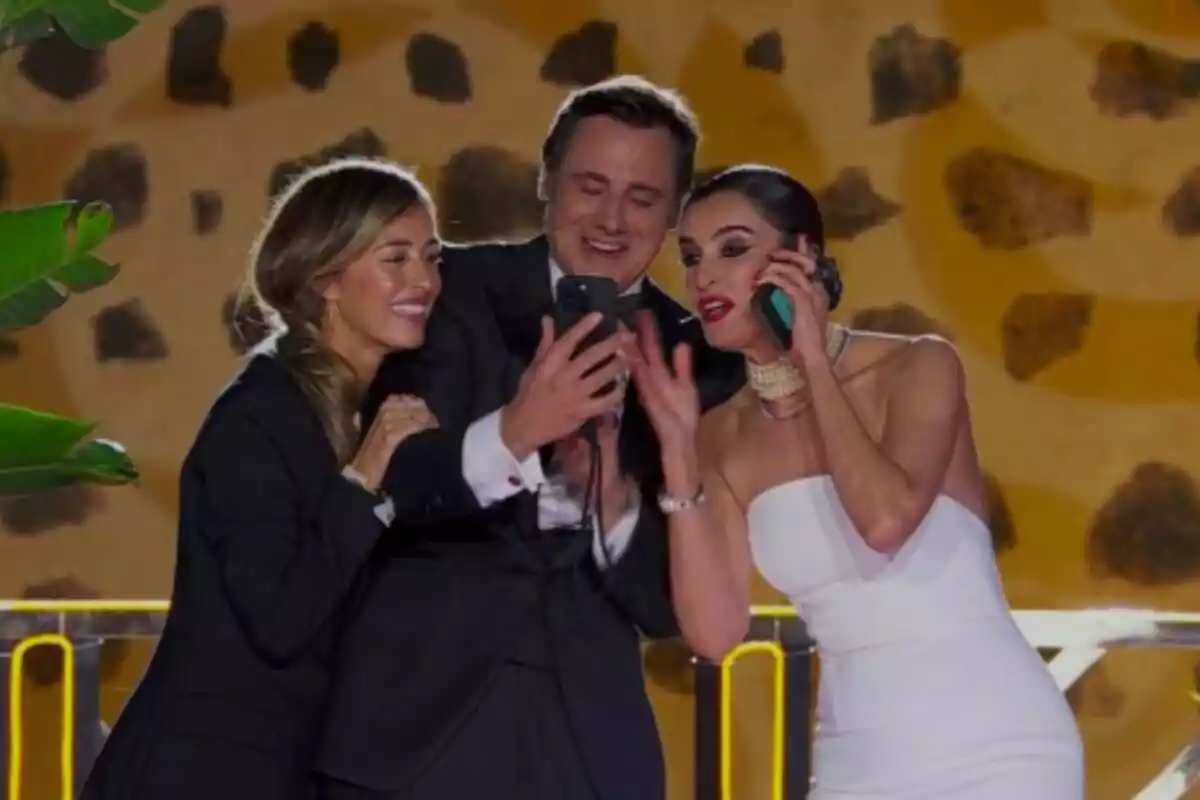 Ion Aramendi i la seva dona María Amores amb Blanca Romero somriuen mentre miren un telèfon mòbil en un esdeveniment elegant a les Campanades. Ion Aramendi i la seva dona María Amores amb Blanca Romero somriuen mentre miren un telèfon mòbil en un esdeveniment elegant a les Campanades.