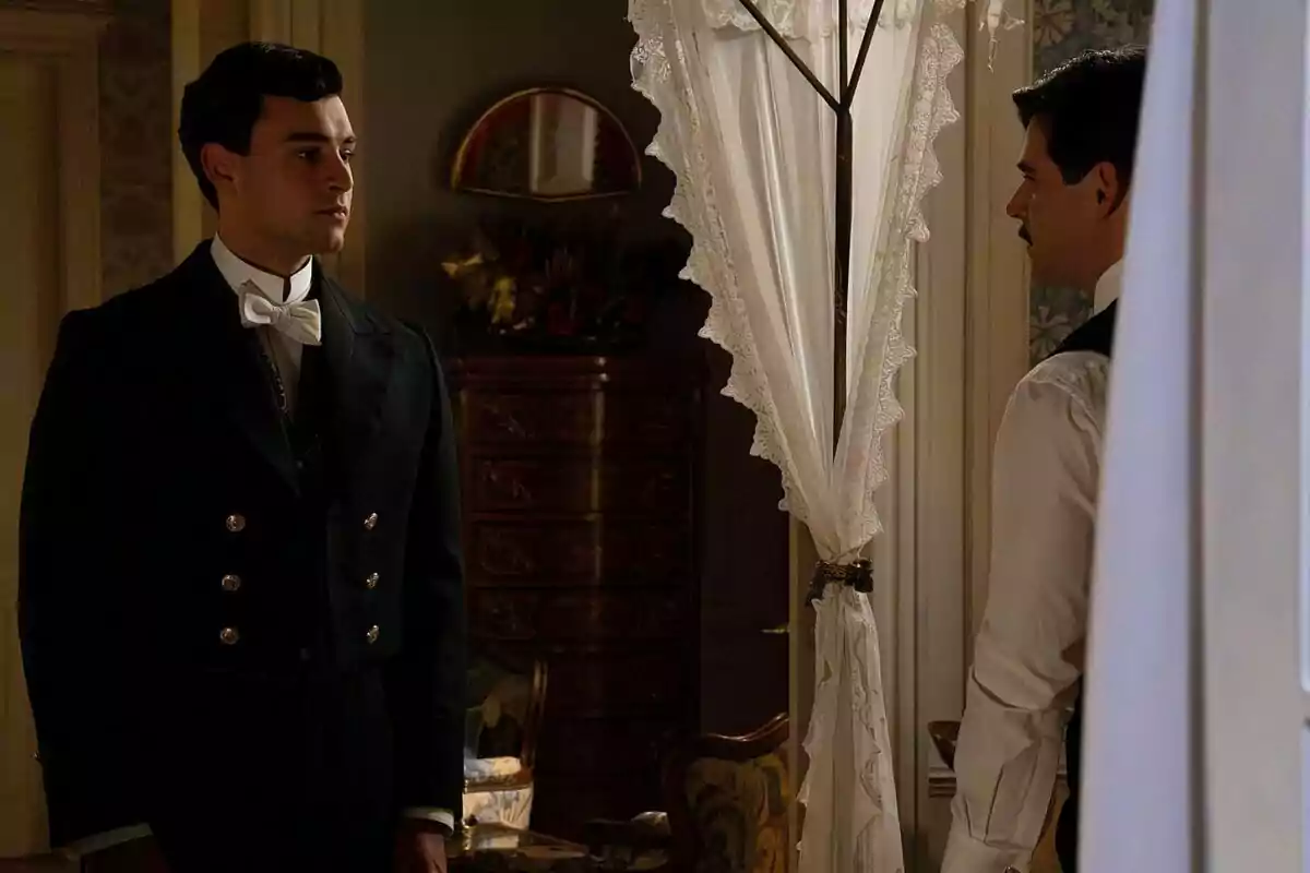 Xavi Lock i Arturo Sancho vestits de manera elegant es troben en una habitació decorada amb mobles clàssics i cortines de puntes a La Promesa.