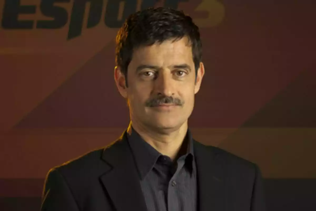 Xavier Bonastre con bigote y cabello oscuro lleva un traje oscuro y camisa azul frente a un fondo con el logo de Esport3.