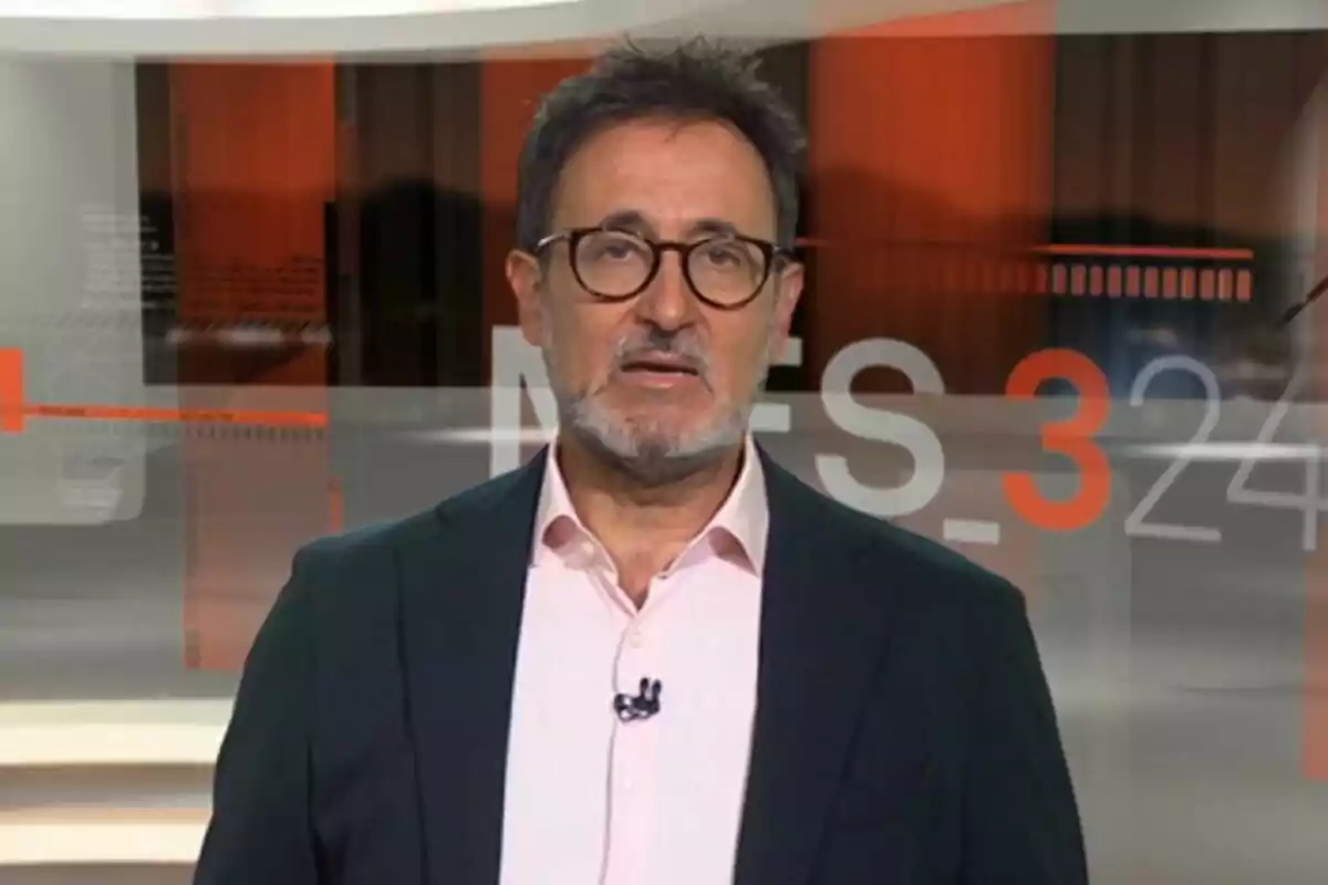 Captura de Xavier Grasset con gafas y barba hablando frente a un fondo de noticias del 3/24 Captura de Xavier Grasset con gafas y barba hablando frente a un fondo de noticias del 3/24