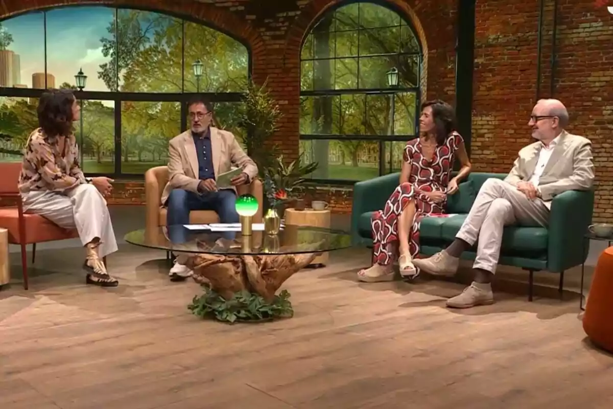 Xavier Grasset junto a Antoni Bassas, Alba Alfageme y Maria Juan sentadas en un set de televisión con una mesa de centro de cristal y un fondo que simula un parque en La Selva. Xavier Grasset junto a Antoni Bassas, Alba Alfageme y Maria Juan sentadas en un set de televisión con una mesa de centro de cristal y un fondo que simula un parque en La Selva.