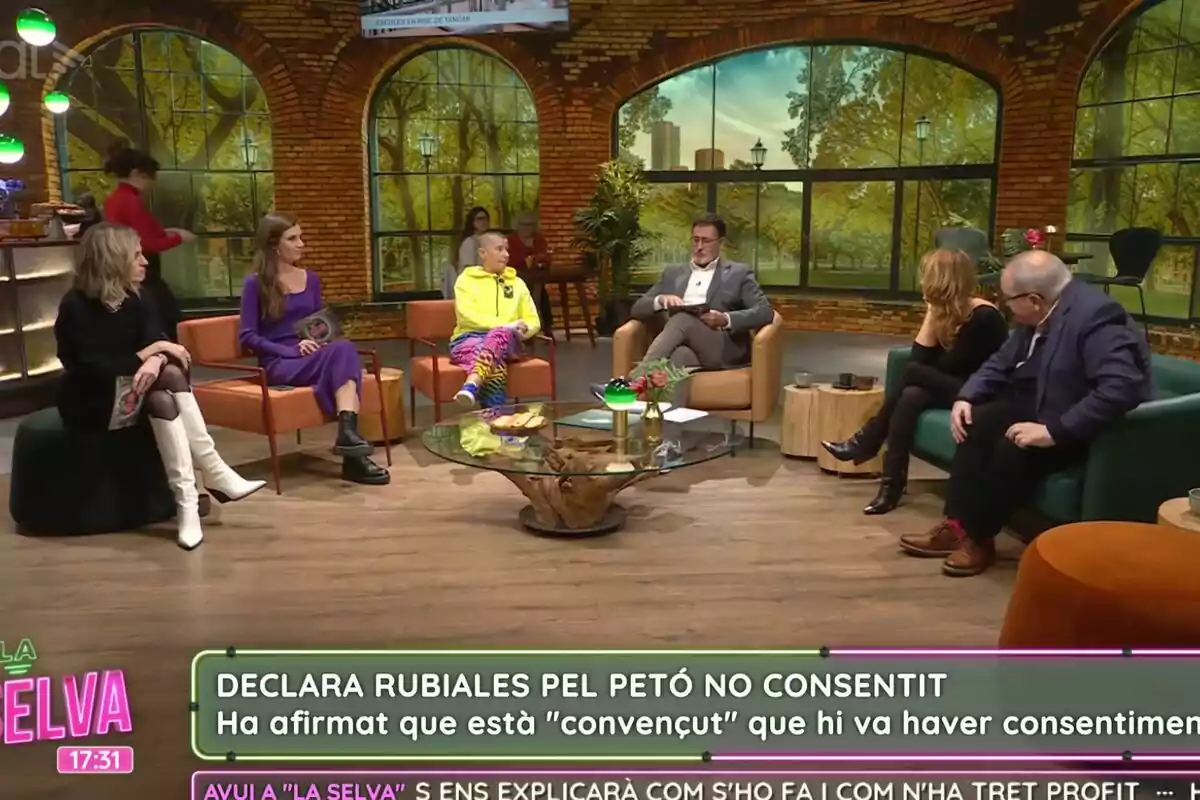 Un grup de persones com Xavier Grasset i María Xinxó està assegut a La Selva, participant en un programa d'entrevistes amb una decoració que simula un entorn natural.
