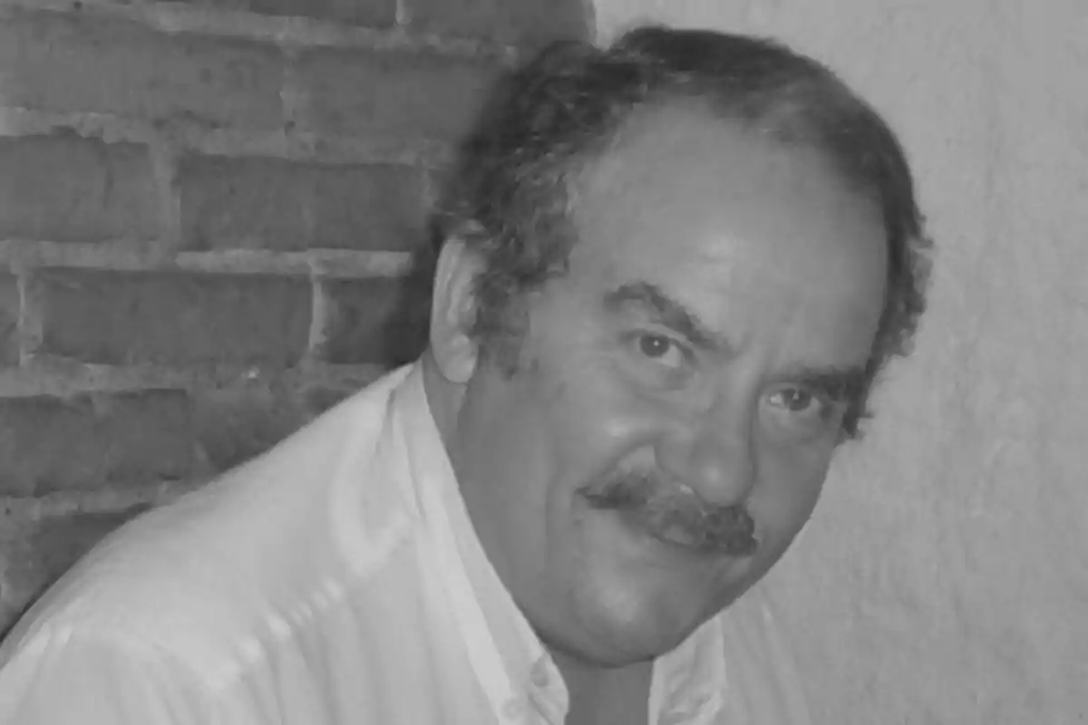 Xavier Serrat gran amb bigoti somriu mentre està dret davant d'una paret de maons.