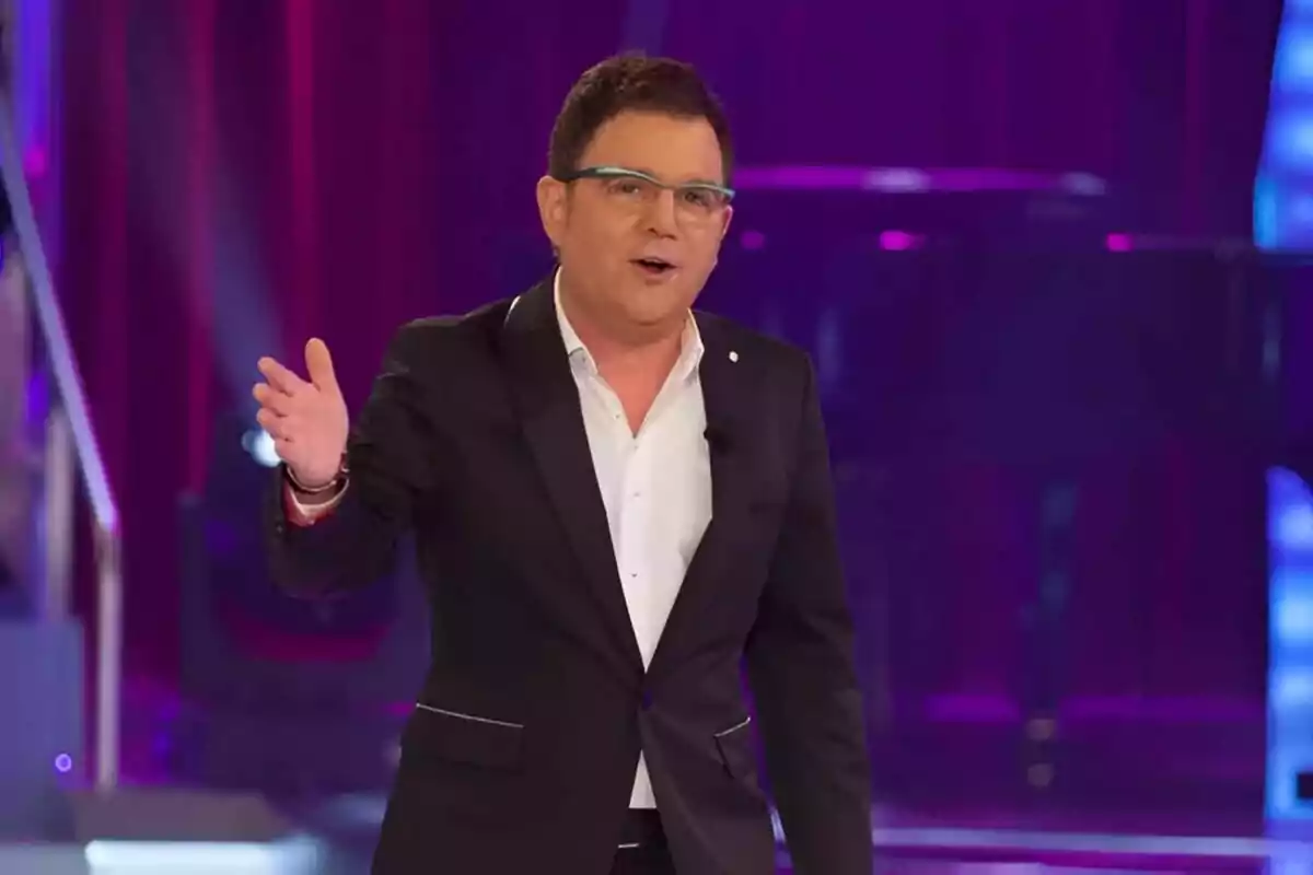 Xosé Manuel Piñeiro amb ulleres i vestit fosc gesticula mentre parla en un escenari il·luminat amb llums de colors.