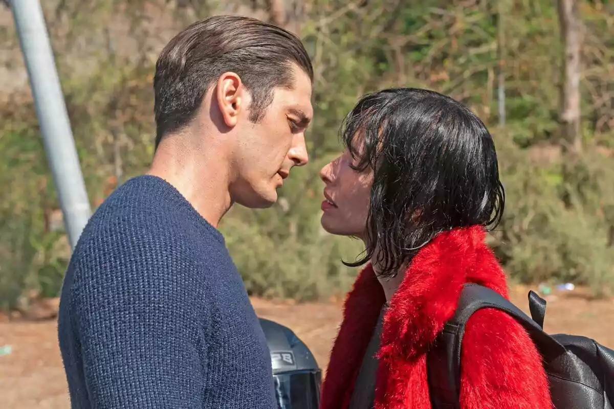 Yon González y Olivia Baglivi mirándose intensamente en un entorno al aire libre, una de ellas lleva un abrigo rojo y una mochila negra en la segunda temporada de Memento Mori.