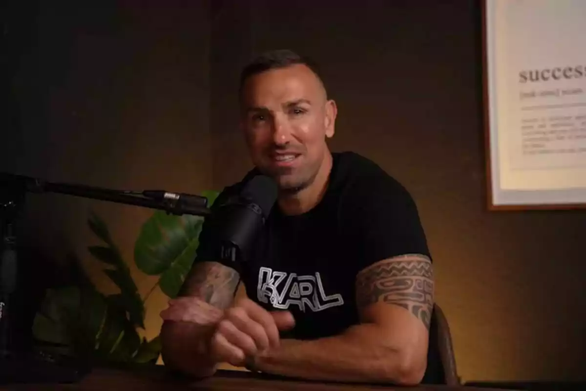 Rafa Mora con tatuajes en los brazos hablando frente a un micrófono en un estudio con una planta y un cuadro en la pared. Captura de YouTube el 24 de junio de 2024 Rafa Mora con tatuajes en los brazos hablando frente a un micrófono en un estudio con una planta y un cuadro en la pared. Captura de YouTube el 24 de junio de 2024